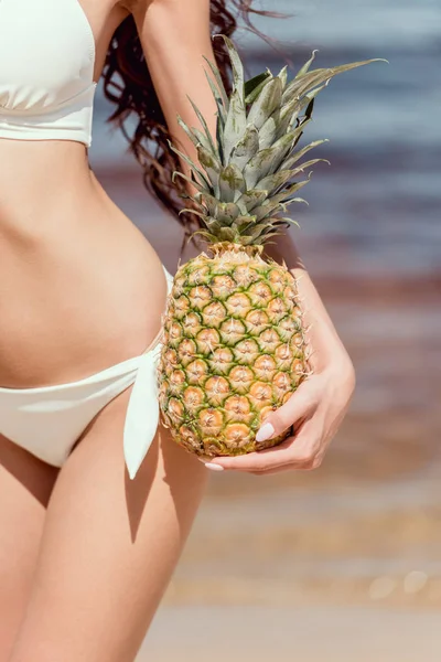 Primer plano de mujer en bikini sosteniendo piña fresca cerca del mar - foto de stock