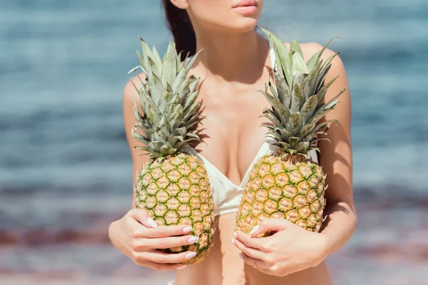 Vue partielle de la femme en maillot blanc tenant des ananas frais près de la mer — Photo de stock