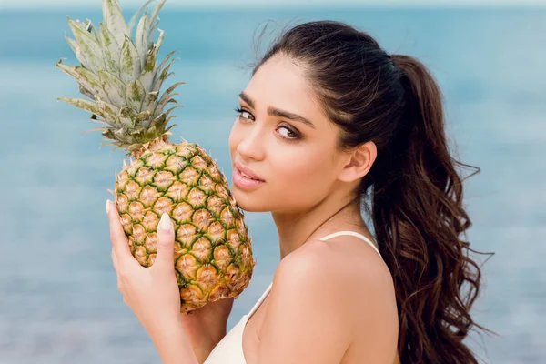 Ritratto di giovane donna attraente che tiene dolce ananas vicino al mare — Foto stock