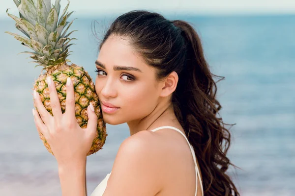 Portrait of young woman in swimsuit holding pineapple near the sea — Stock Photo