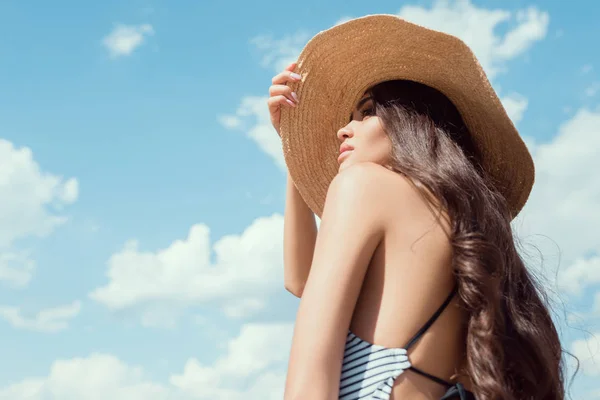 Attractive brunette girl posing in straw hat with blue sky on background — Stock Photo