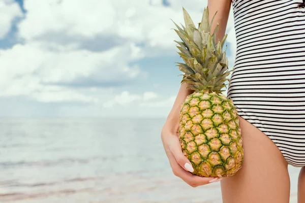 Cropped view of woman in swimsuit holding fresh pineapple near the sea — Stock Photo