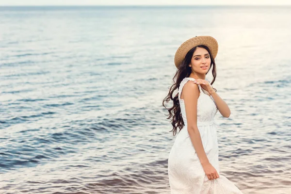 Приваблива дівчина в солом'яному капелюсі, що йде біля моря влітку — стокове фото