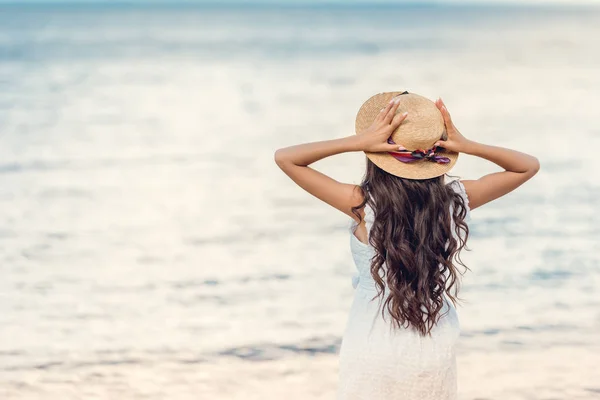 Rückansicht eines Mädchens mit Strohhut, das aufs Meer blickt — Stockfoto
