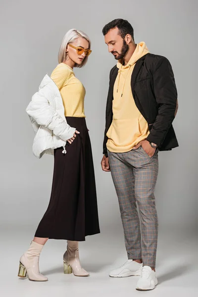 Elegante joven hombre y mujer en trajes de otoño posando sobre fondo gris - foto de stock