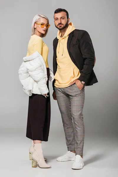 Young couple of models in stylish autumn outfits posing on grey background — Stock Photo