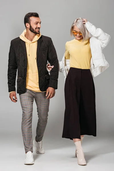 Улыбающаяся пара стильных моделей в осенних нарядах на сером фоне — стоковое фото