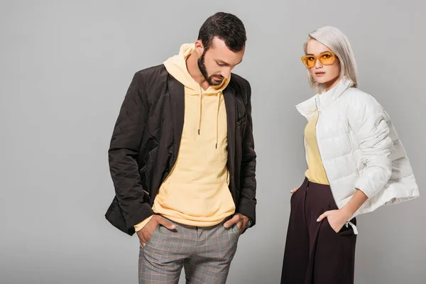 Casal elegante de modelos posando com as mãos em bolsos isolados no fundo cinza — Fotografia de Stock