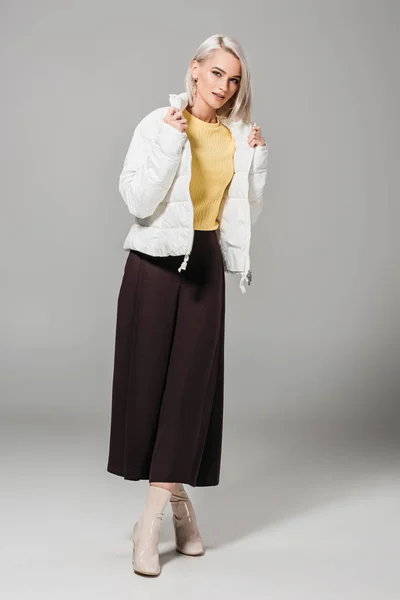 Приваблива жіноча модель в стильній білій куртці позує на сірому фоні — стокове фото