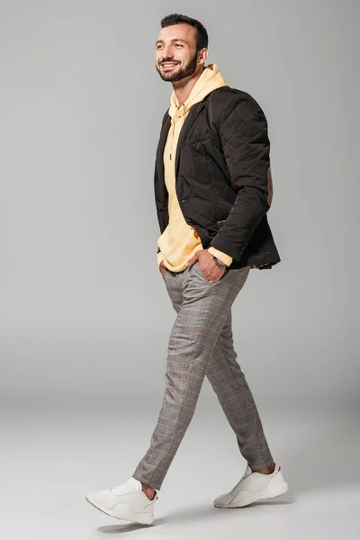 Modèle masculin élégant et souriant en tenue d'automne posant avec les mains dans les poches sur fond gris — Photo de stock