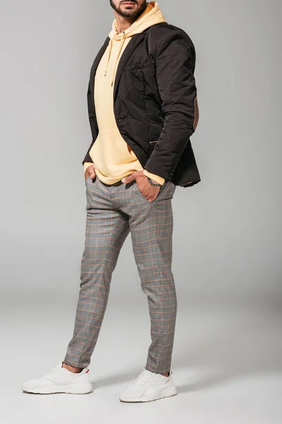 Cropped image of man in fashionable autumn outfit posing with hands in pockets on grey background — Stock Photo
