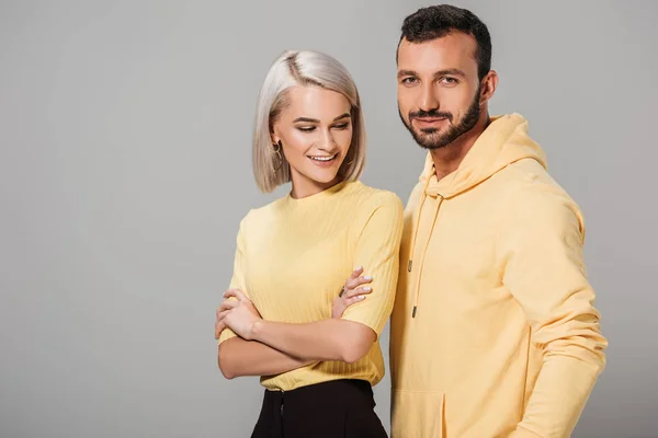 Smiling woman with crossed arms posing in yellow clothes with boyfriend isolated on grey — Stock Photo