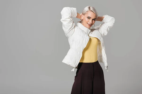 Happy female model in stylish autumn jacket posing with raised arms isolated on grey background — Stock Photo