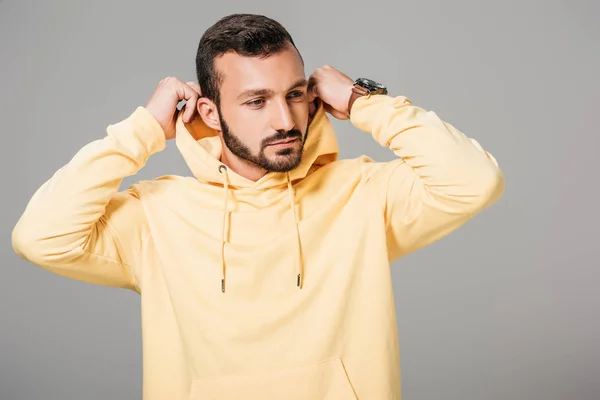 Handsome bearded male model putting on yellow hoodie isolated on grey background — Stock Photo