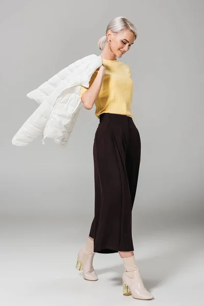 Lächelndes weibliches Modell mit Jacke über der Schulter isoliert auf grauem Hintergrund — Stockfoto
