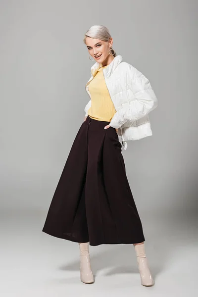 Lächelndes weibliches Model in stylischem Outfit posiert mit den Händen an der Taille auf grauem Hintergrund — Stockfoto