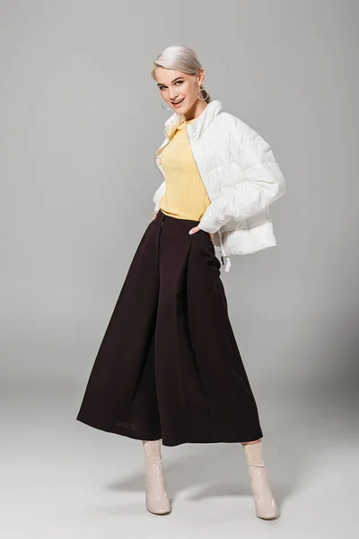 Modelo femenino sonriente en traje elegante posando con las manos en la cintura sobre fondo gris - foto de stock