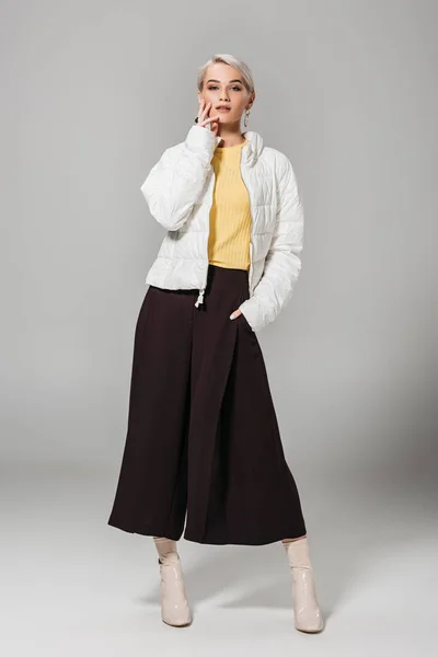Modelo feminino elegante atraente em jaqueta branca posando no fundo cinza — Fotografia de Stock