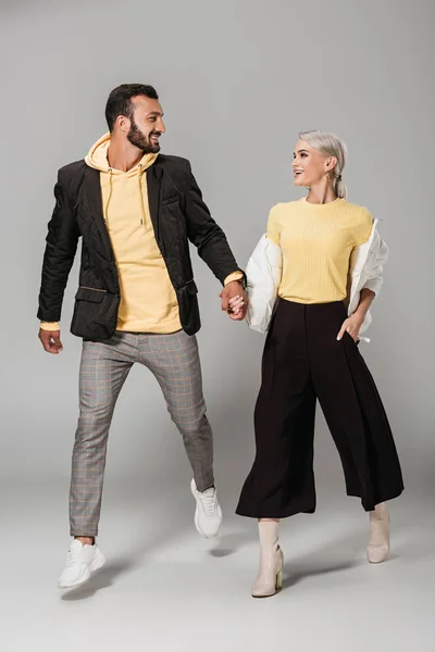 Fashionable couple of models holding hands and looking at each other on grey background — Stock Photo