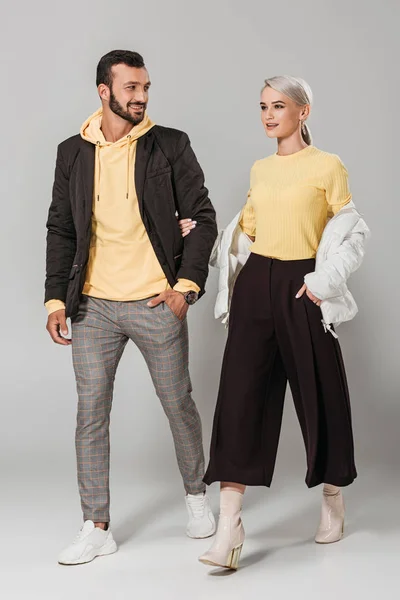 Улыбающаяся пара моделей в стильных осенних нарядах на сером фоне — стоковое фото