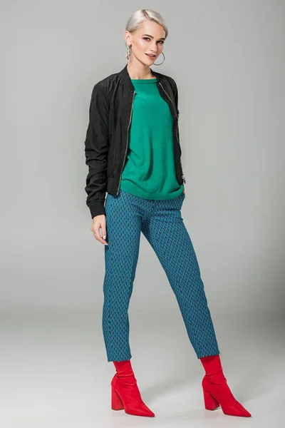 Усміхнена стильна жіноча модель в осінньому вбранні позує на сірому фоні — стокове фото