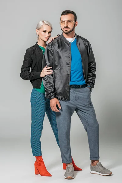 Красива чоловіча модель в осінньому вбранні позує біля стильної дівчини на сірому фоні — стокове фото