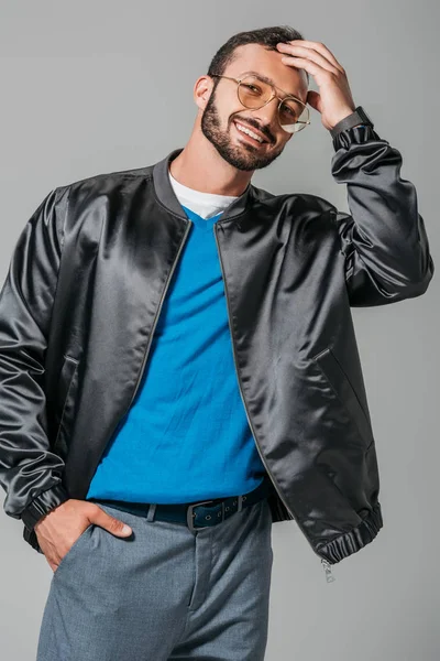 Усміхнена чоловіча модель в стильному чорному бомбардувальнику позує з рукою в кишені ізольовано на сірому фоні — стокове фото