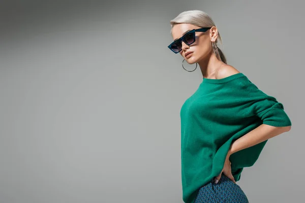 Модная молодая женщина в солнечных очках позирует с руками на талии изолированы на сером фоне — стоковое фото