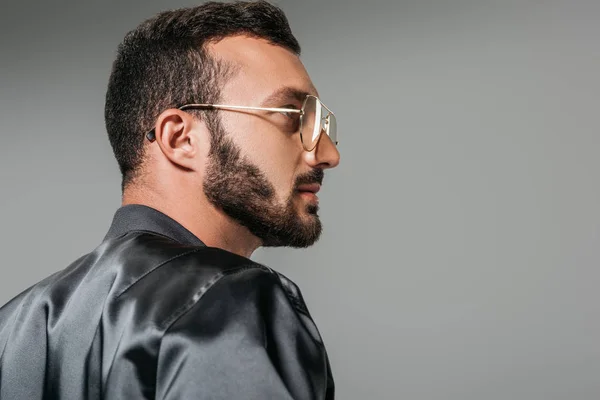 Vue latérale de l'homme barbu dans des lunettes élégantes et bombardier noir isolé sur fond gris — Photo de stock