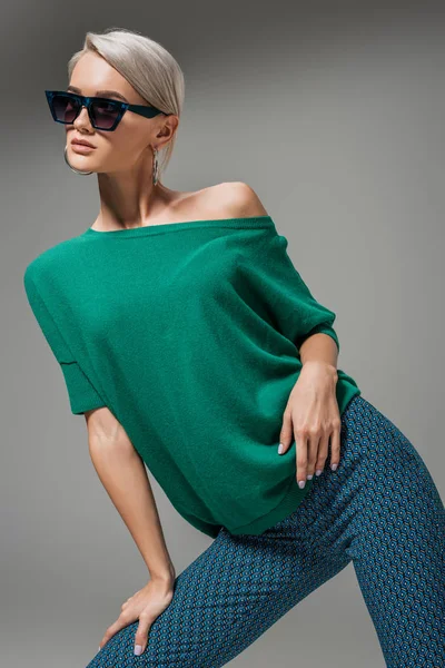 Jovem modelo feminino em óculos de sol e suéter verde posando isolado em fundo cinza — Fotografia de Stock