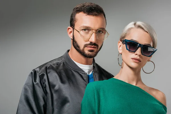 Модная пара, позирующая в очках и солнцезащитных очках, изолированная на сером — стоковое фото