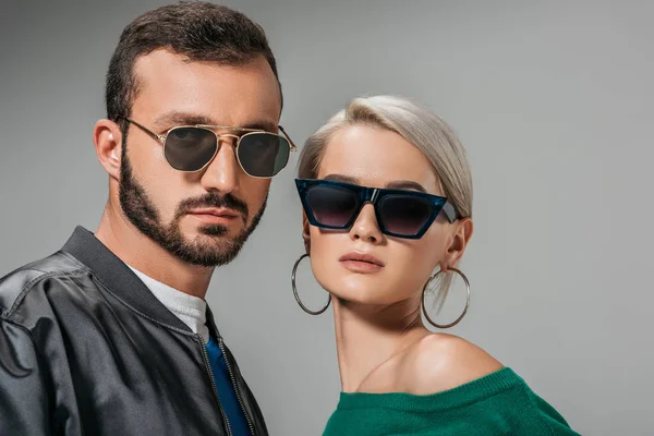 Модная пара, позирующая в модных солнцезащитных очках, изолированная на сером — стоковое фото
