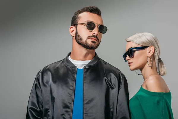 Couple à la mode posant dans des lunettes de soleil, isolé sur gris — Photo de stock