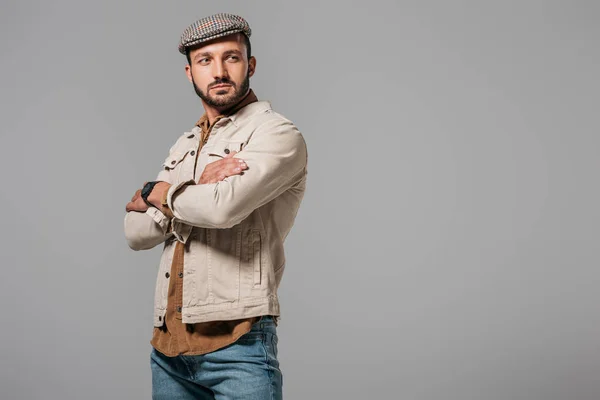 Hombre guapo en chaqueta de otoño y gorra de tweed posando con los brazos cruzados, aislado en gris - foto de stock