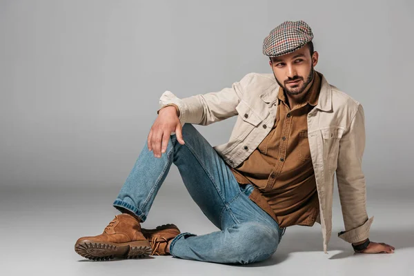 Hombre barbudo posando en camisa de pana, jeans y chaqueta de otoño y gorra de tweed, sobre gris - foto de stock