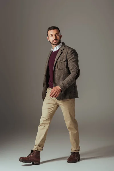 Стильный мужчина позирует в бежевых штанах и осенней твидовой куртке, на сером — стоковое фото