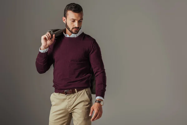 Stylish handsome man posing in burgundy sweater with jacket on shoulder, isolated on grey — Stock Photo