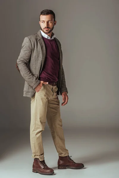 Бородатый мужчина позирует в стильной осенней твидовой куртке, на сером — стоковое фото