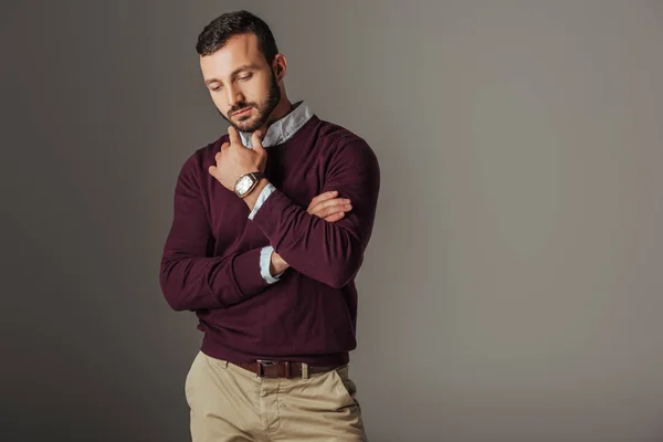 Вдумчивый красивый мужчина-модель позирует в бордовом свитере, изолированный на сером — стоковое фото