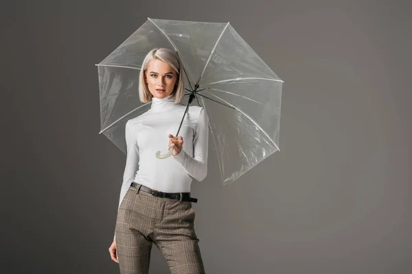 Elegant model in white turtleneck with transparent umbrella, isolated on grey — Stock Photo