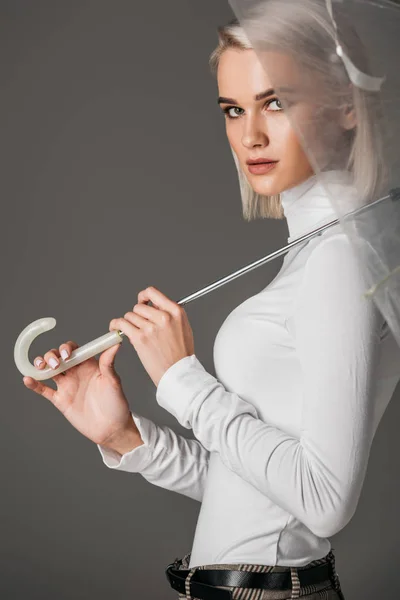 Élégante fille à col roulé blanc posant avec parapluie transparent tendance, isolé sur gris — Photo de stock