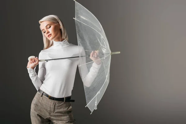 Femme à col roulé blanc posant avec parapluie transparent automne, isolé sur gris — Photo de stock