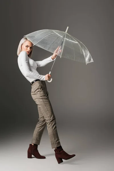 Confused girl in white turtleneck with transparent umbrella, on grey — Stock Photo