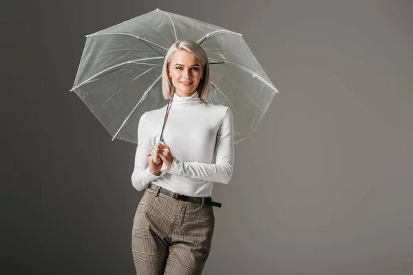 Beautiful girl in white turtleneck posing with transparent umbrella, isolated on grey — Stock Photo