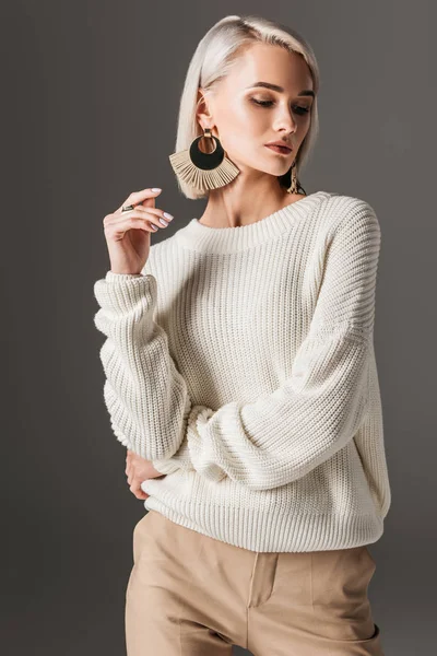Приваблива елегантна жінка позує в білому светрі і великих сережках, ізольована на сірому — Stock Photo