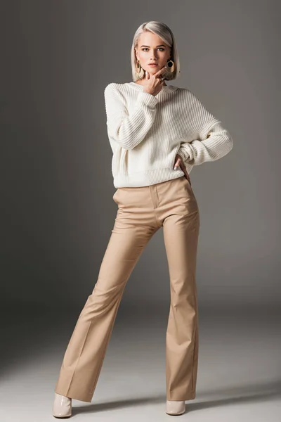 Elegant fashionable woman posing in white sweater and beige pants, on grey — Stock Photo