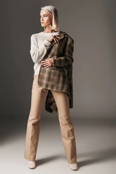 Stylish elegant model posing in autumn sweater, beige pants and tweed jacket, on grey — Stock Photo