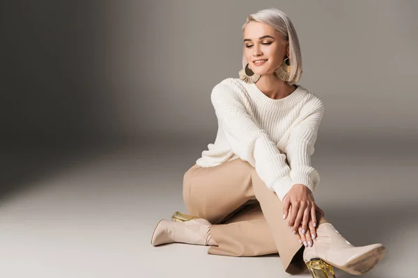 Усміхнена елегантна модель позує в білому светрі, бежеві штани і осінні підбори, на сірому — стокове фото
