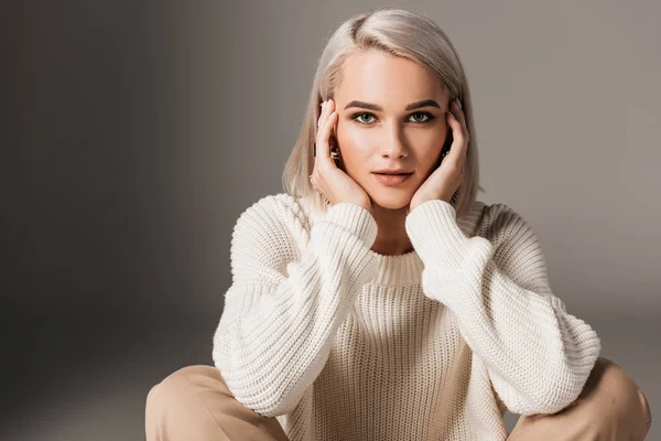 Felice ragazza elegante seduta in maglione bianco, isolato su grigio — Foto stock