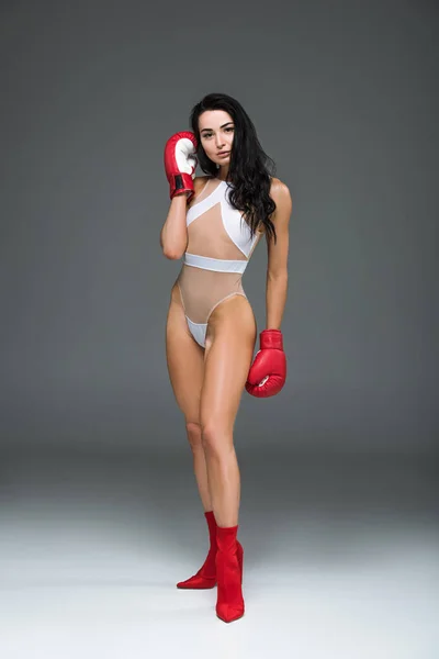 Sexy donna sportiva in costume da bagno bianco e guanti da boxe in piedi, su grigio — Foto stock